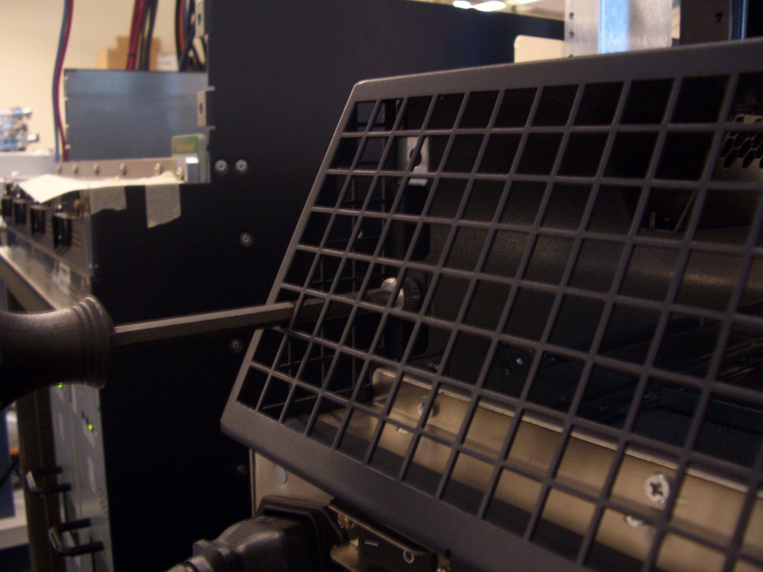 Close-up of a screwdriver adjusting a component on electronic equipment with a grid-like cover in a technical environment.