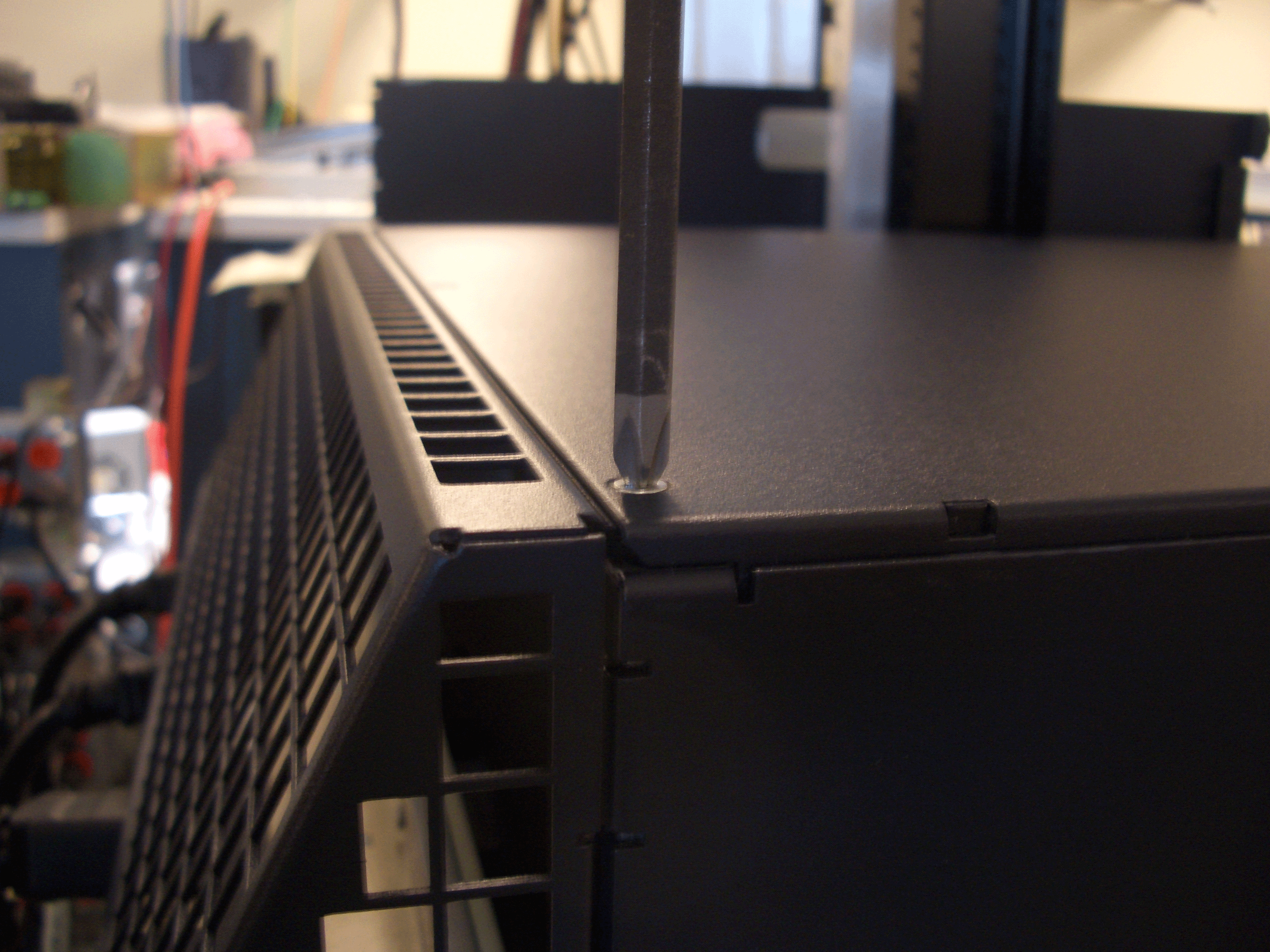 Tightening a screw on a server case top panel with a screwdriver in a workspace.