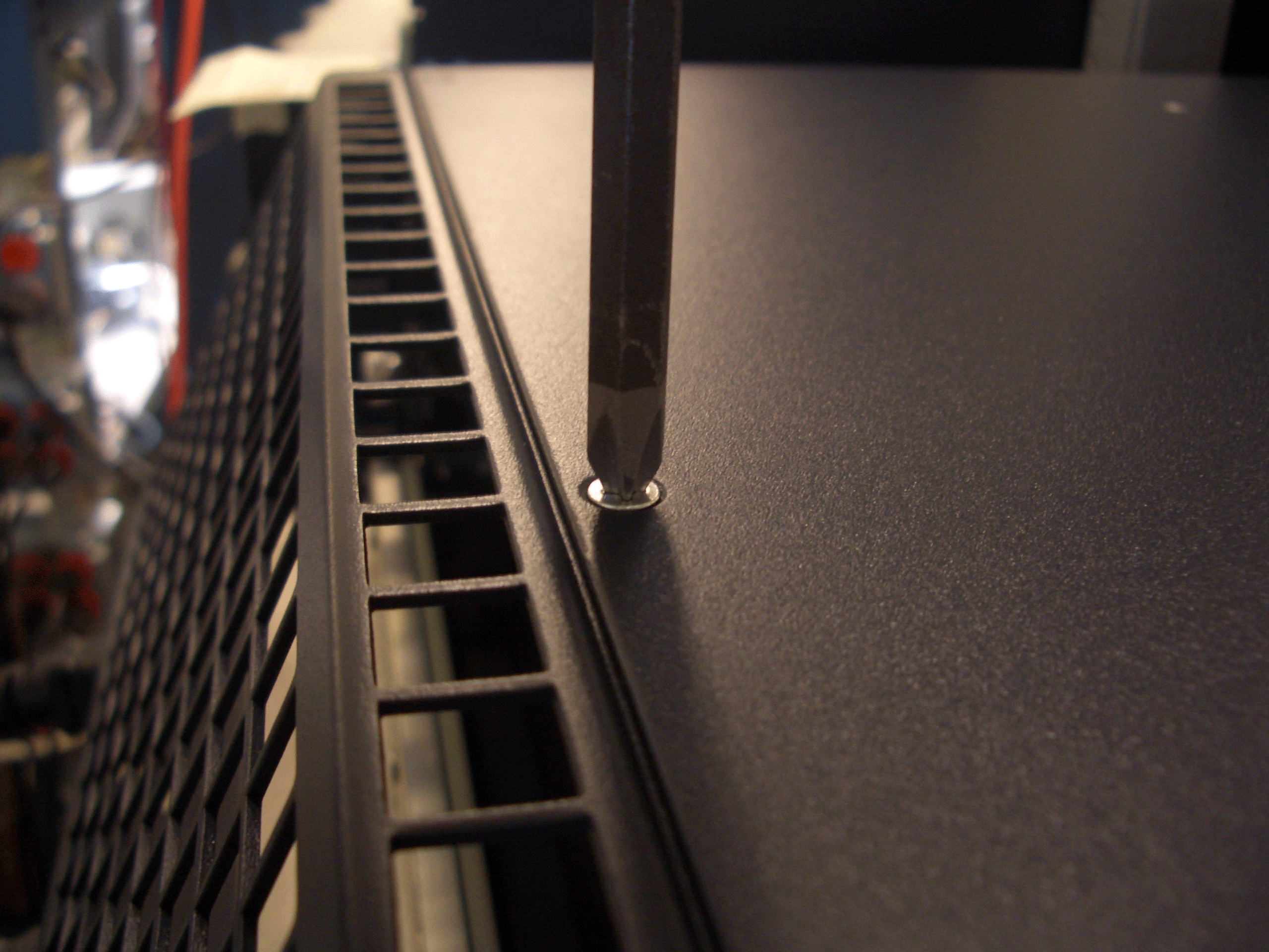 Screwdriver tightening or loosening a screw on a metal surface with vented grille, suggesting a computer case.