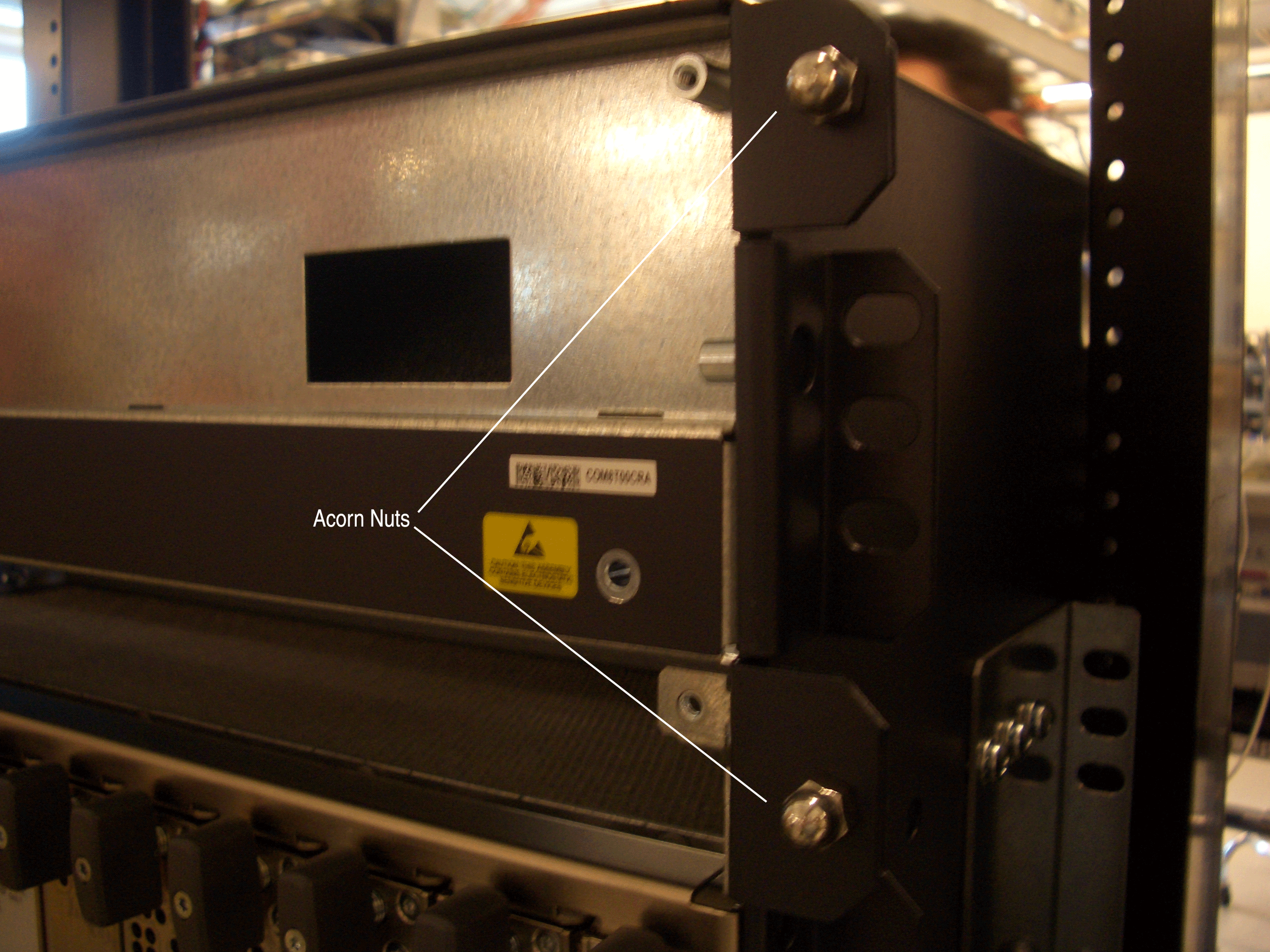 Electronic hardware mounted in a server rack with Acorn Nuts securing it. Metal casing with warning labels and perforated sides for ventilation.