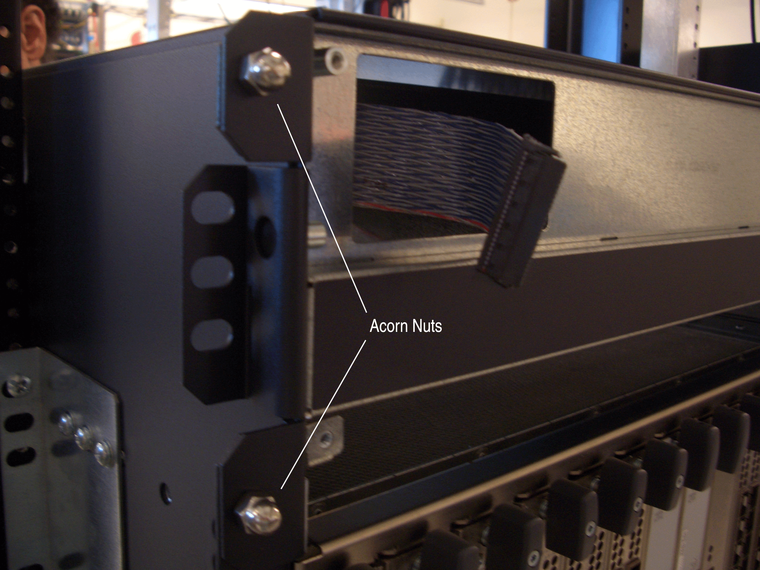 Close-up of server rack showing acorn nuts, ribbon cable, and metal enclosure with rack mounting holes, typical in data centers.