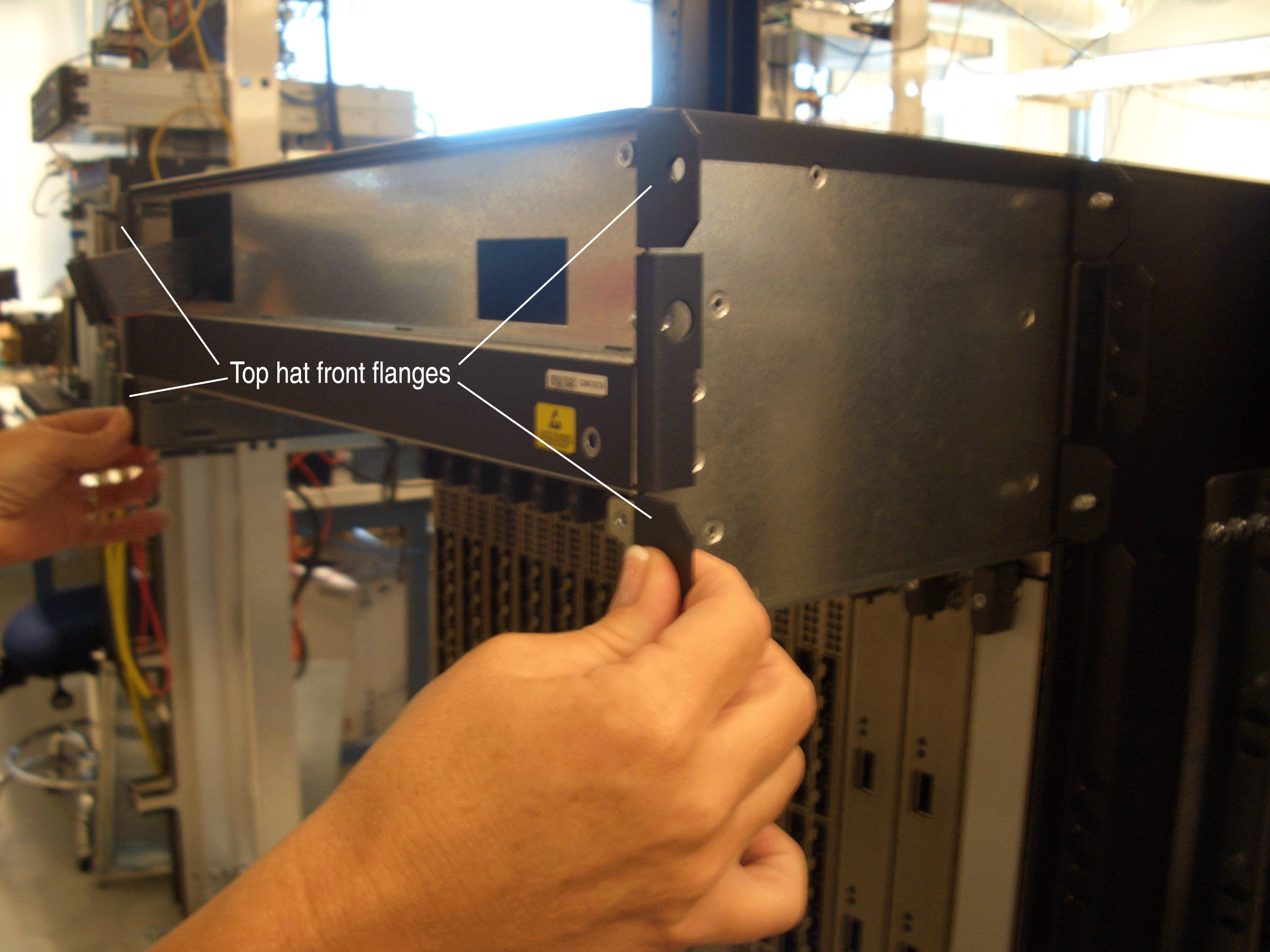 Person handling server equipment with labeled top hat front flanges in a data center environment.