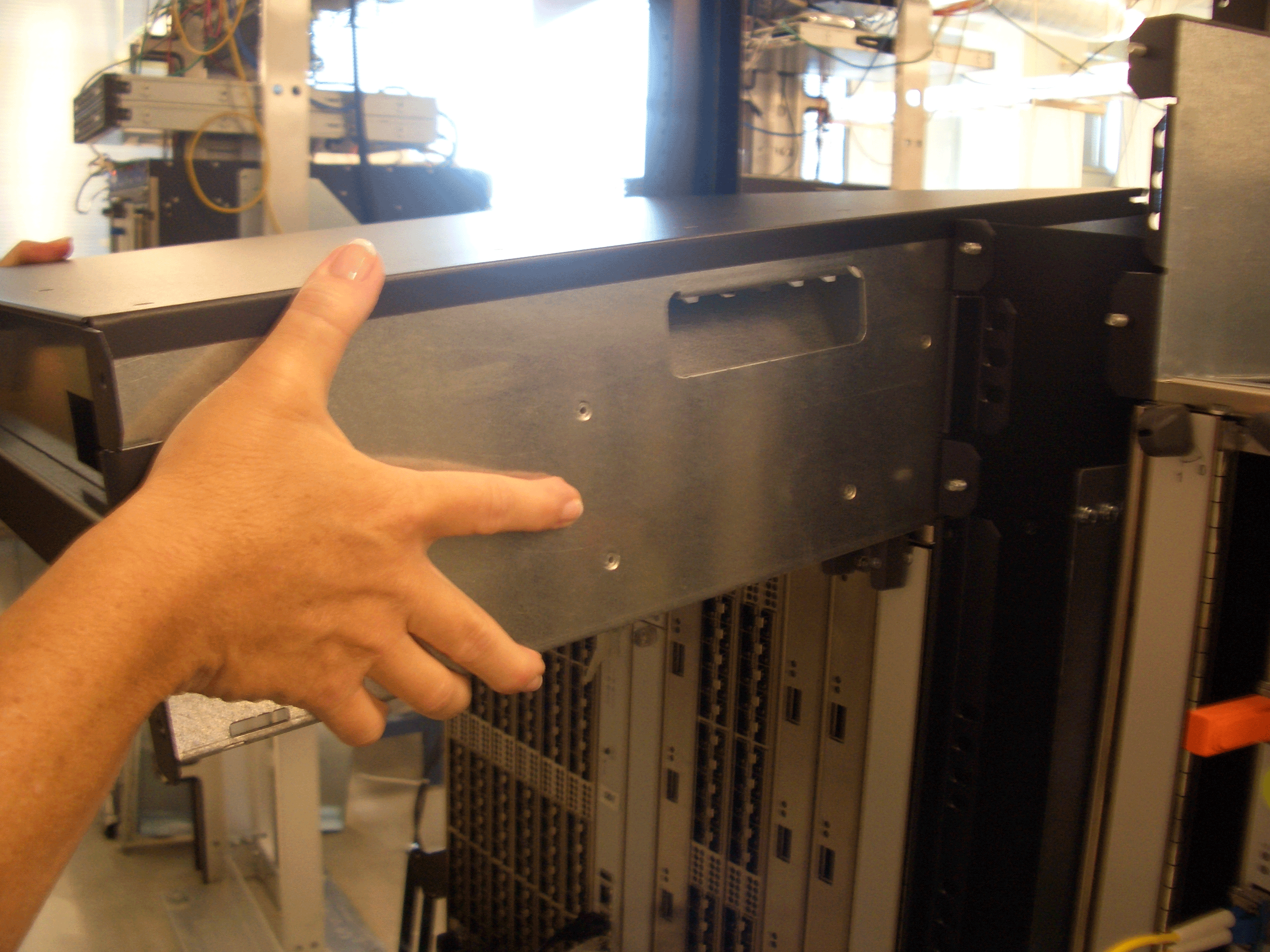 A person handling a server in a data center rack, with visible network equipment and cabling in the background.