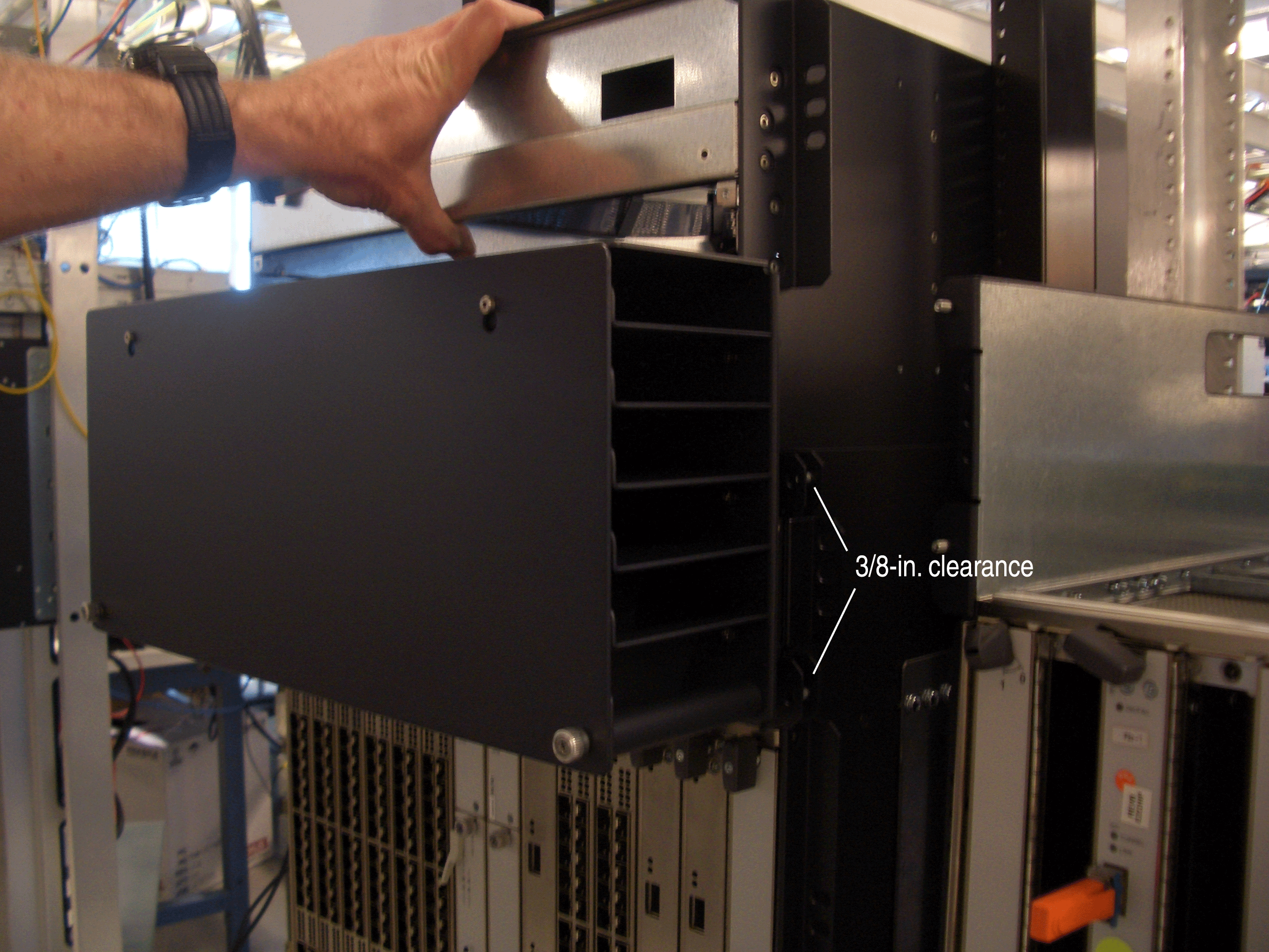 Person installing or removing a black metal component from a server rack with 3/8-in. clearance for airflow.