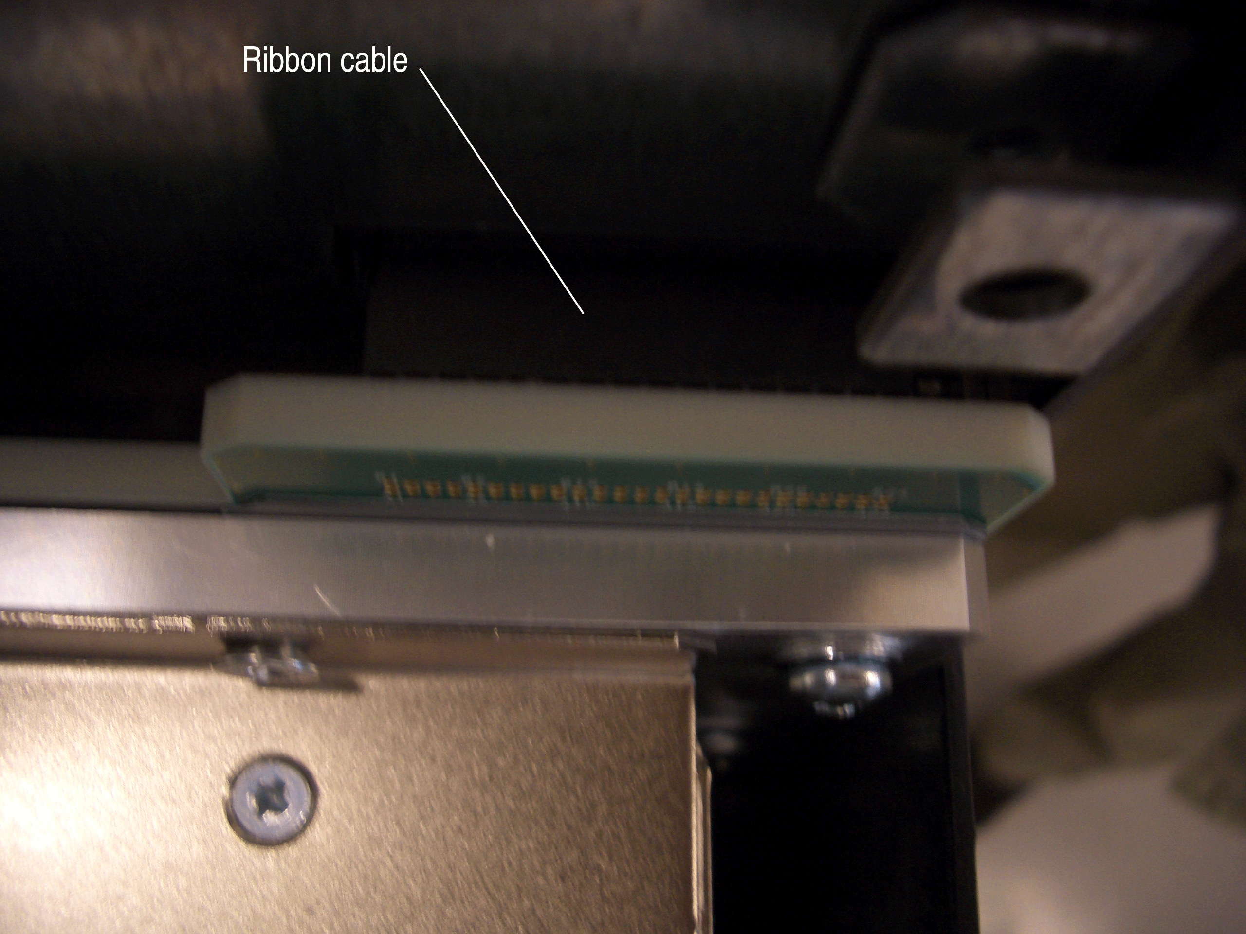 Close-up of a ribbon cable connected to a device, showing screws and metallic parts.