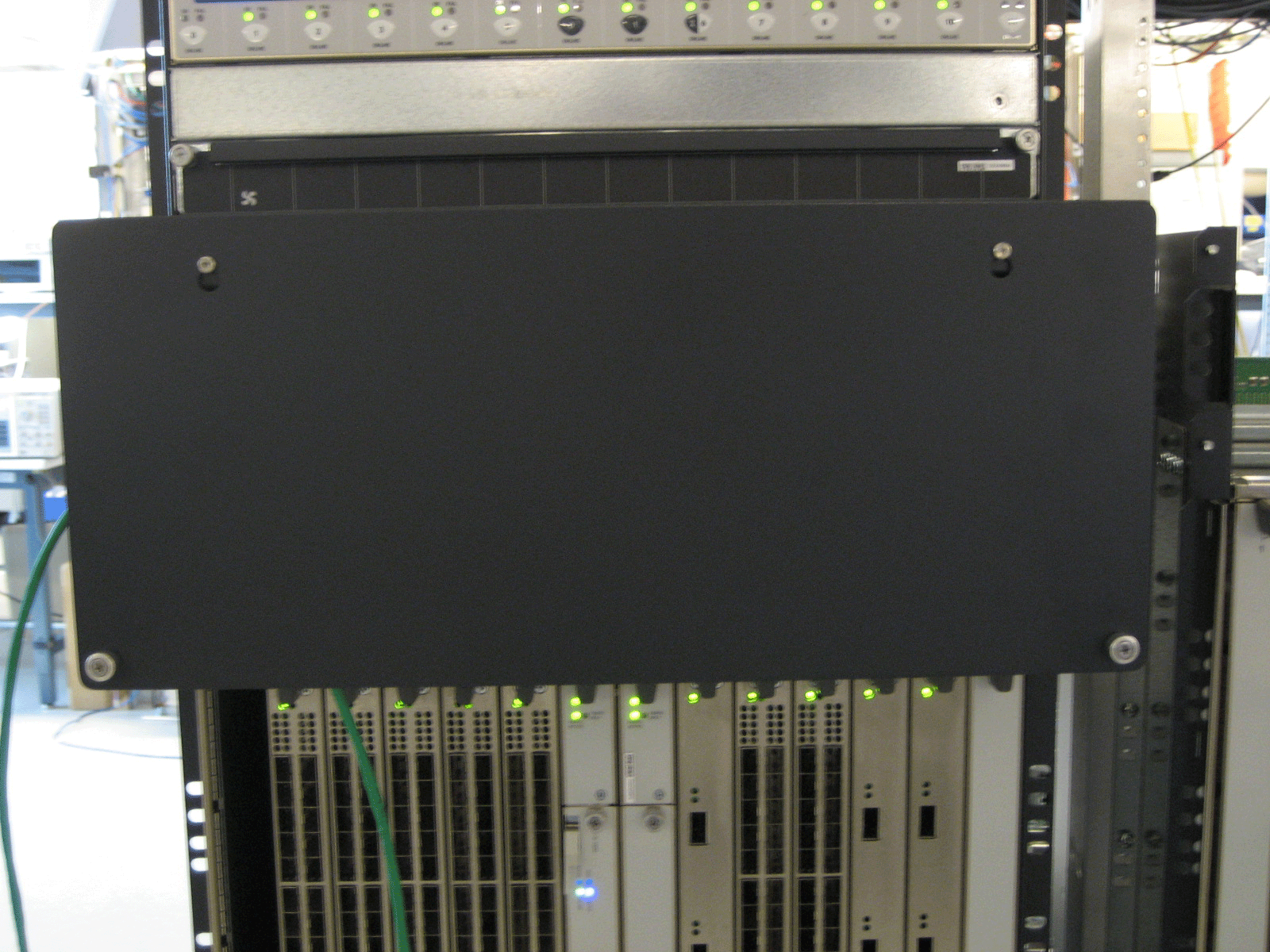 Rack-mounted server equipment with a black protective panel, green cables, and indicator lights in a data center.