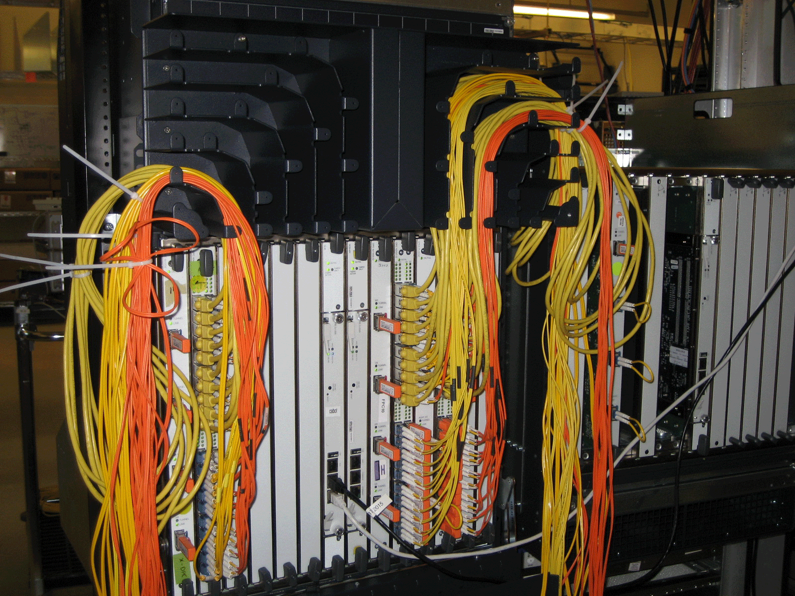 Fiber optic patch panel with yellow and orange cables connected to multiple ports for network management.