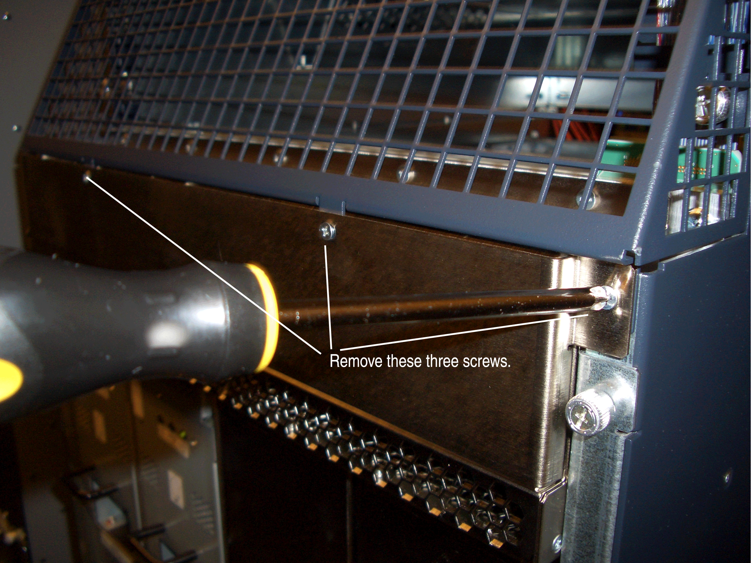 Screwdriver removing screws from a metal panel with mesh grille above it; text instructs to remove three screws.
